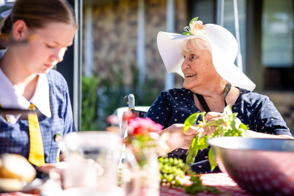 Elderly resident laughing at a table wearing a sun hat.